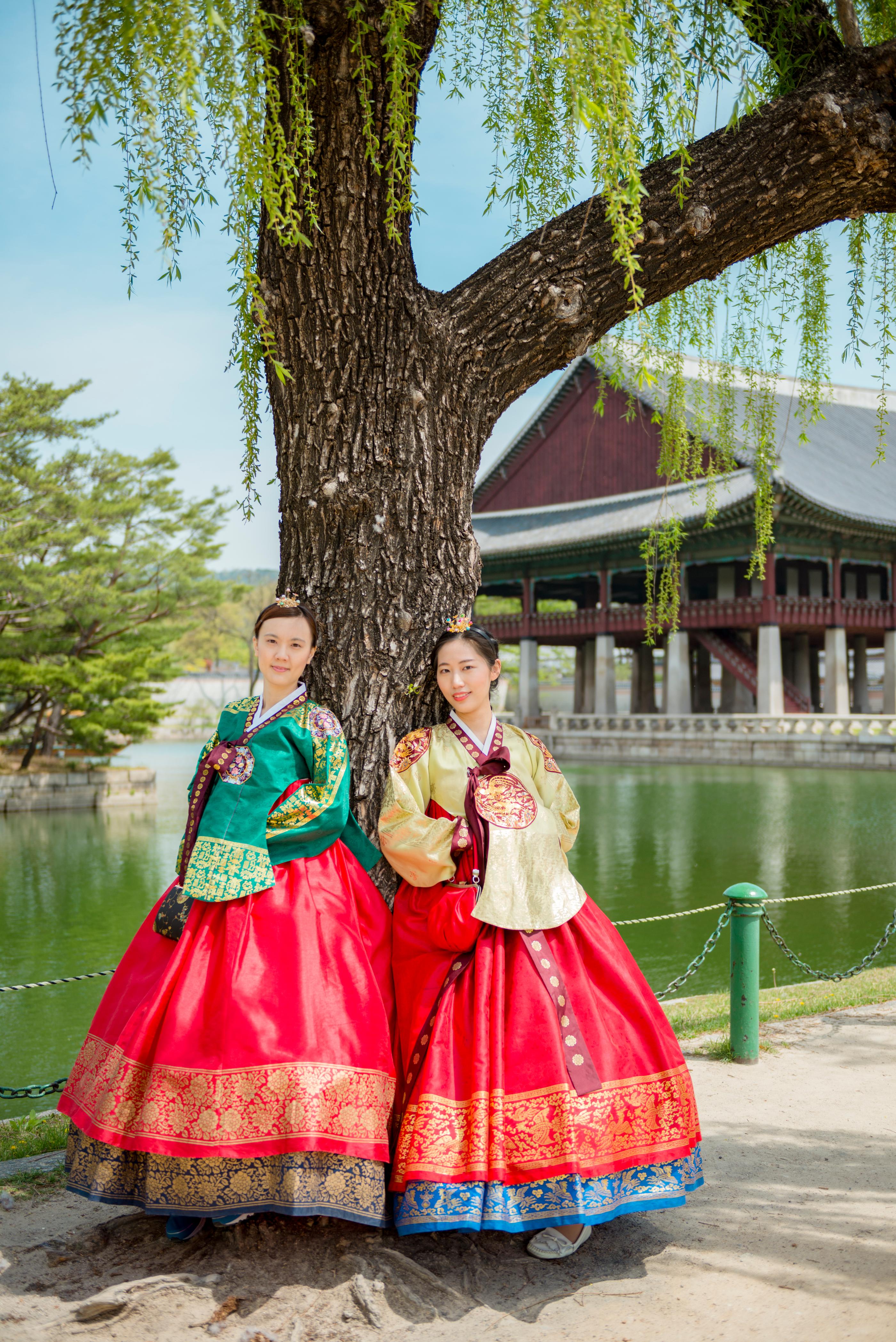 柳の木の下で韓服を着た二人が風景の中で立つ様子