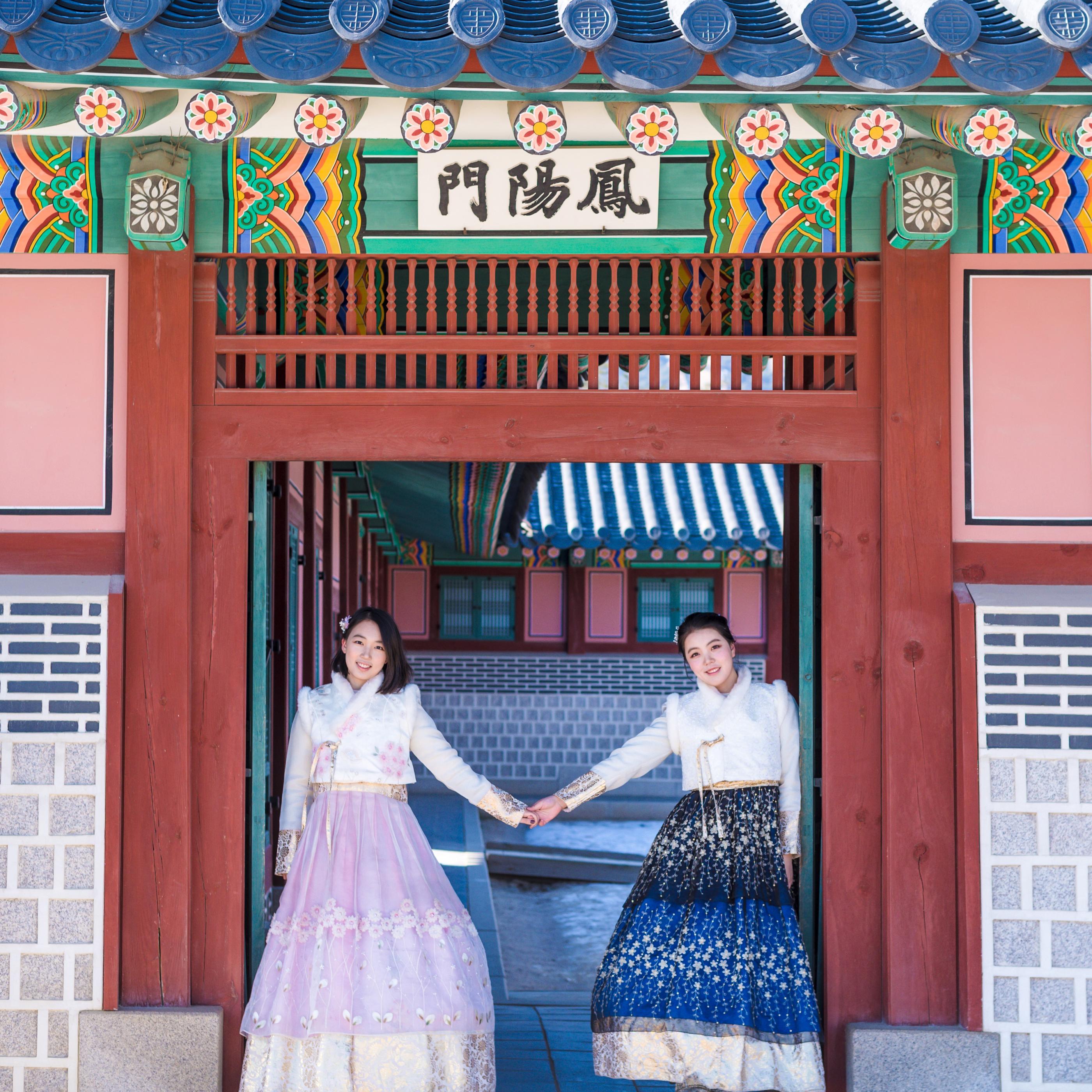 伝統的な韓国の建物の門で韓服姿のカップルがポーズを取る様子