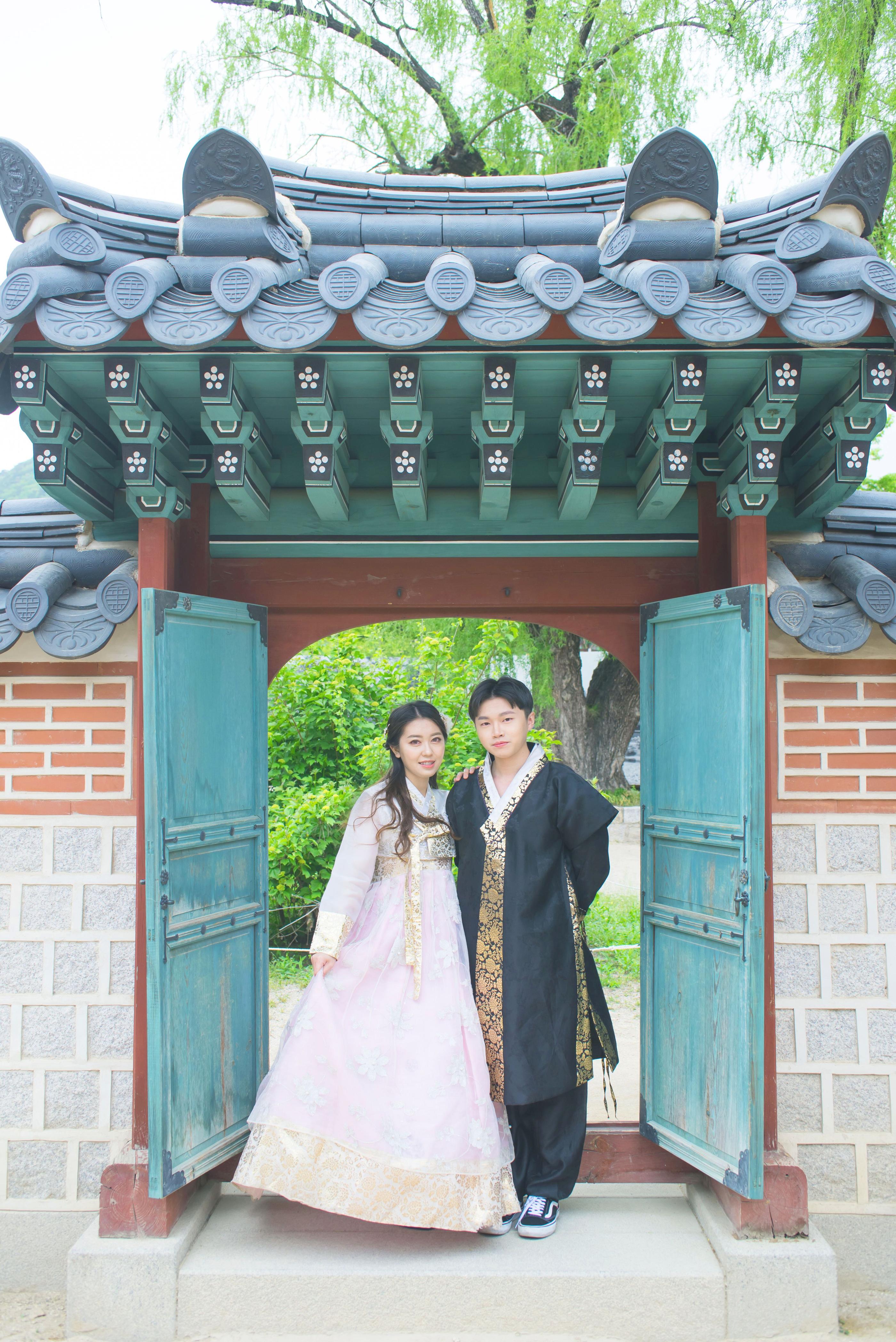 韓国の伝統的な家の門で韓服を着たカップルが立つ姿