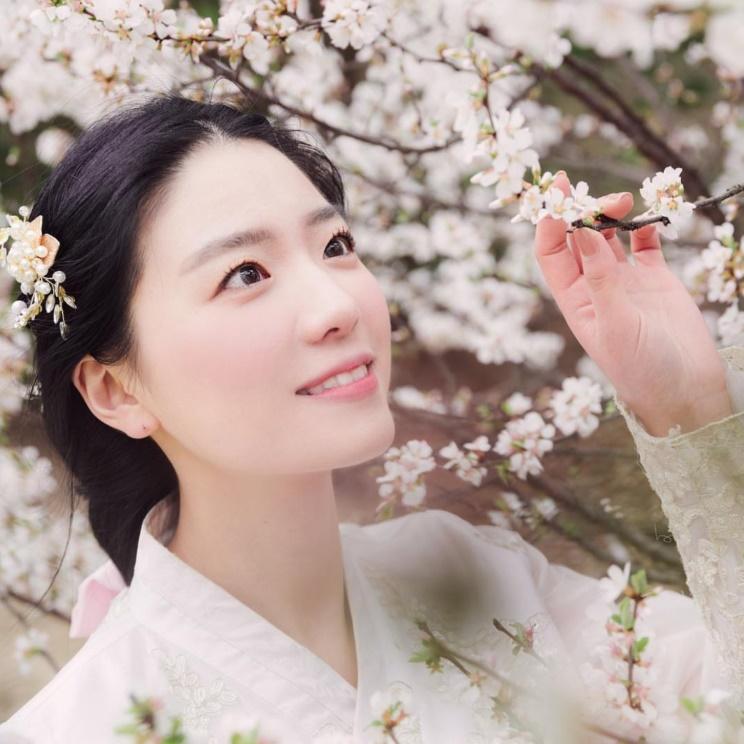 韓国の伝統的な建物の門で赤い韓服を着た女性が扇を持つ姿