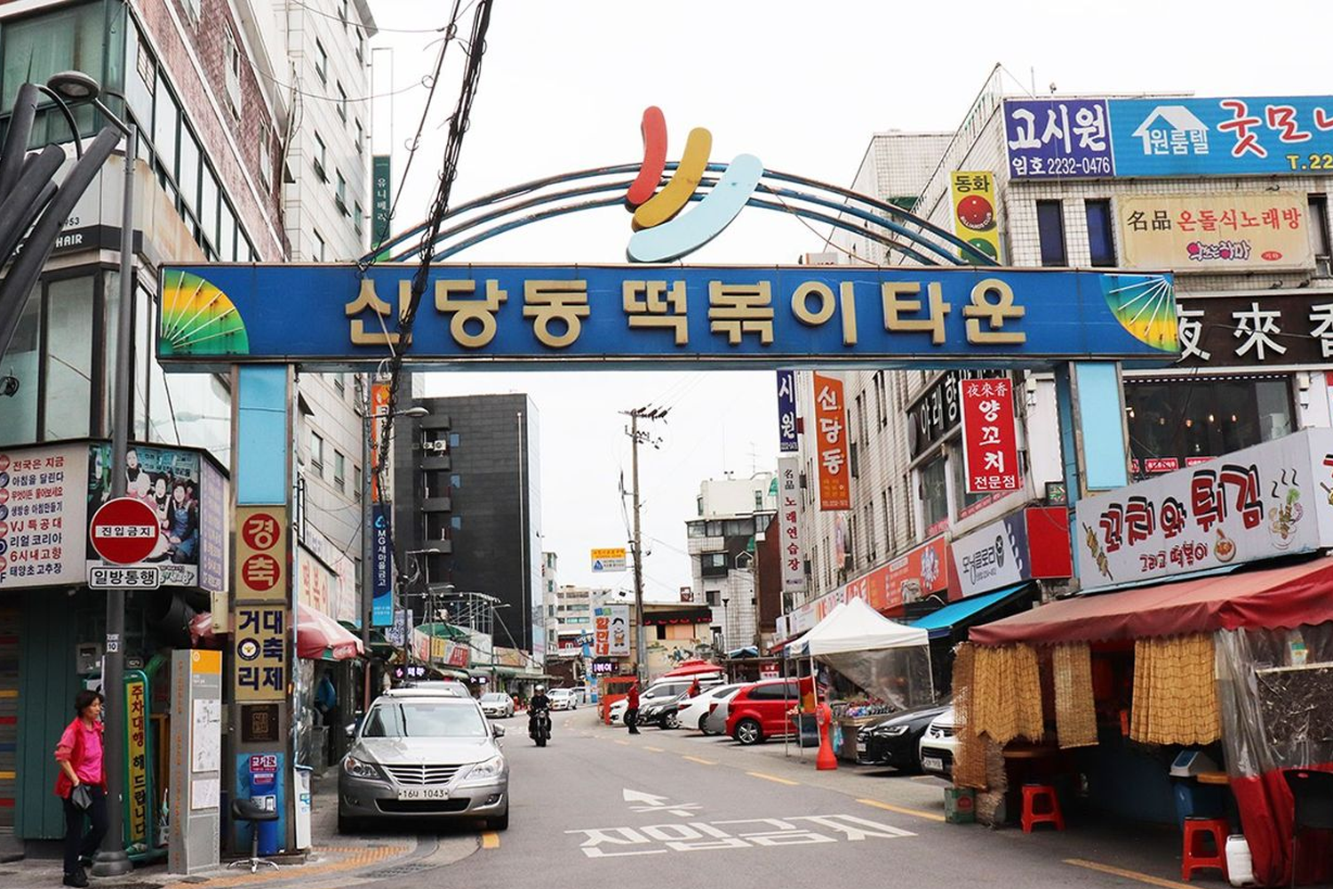 首爾新堂站附近的辣炒年糕街入口，牌子上顯示韓文標識，左右兩側商店林立，是品嚐韓國街頭小吃的好去處。
