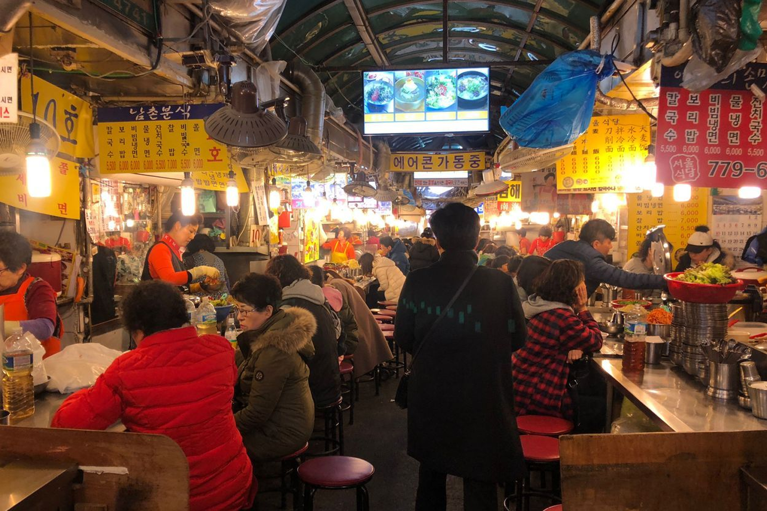 南大門市場的刀削麵小食街，熱鬧的市場氛圍讓遊客們流連忘返，尋找新鮮的韓式街頭美食。