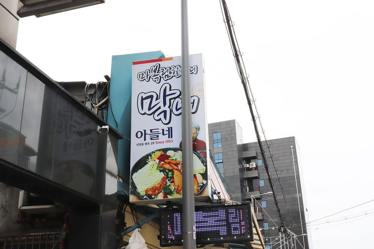 新堂洞的著名辣炒年糕店招牌，裝飾簡單但氛圍熱鬧，吸引了大量食客前來品嚐其特色美食。