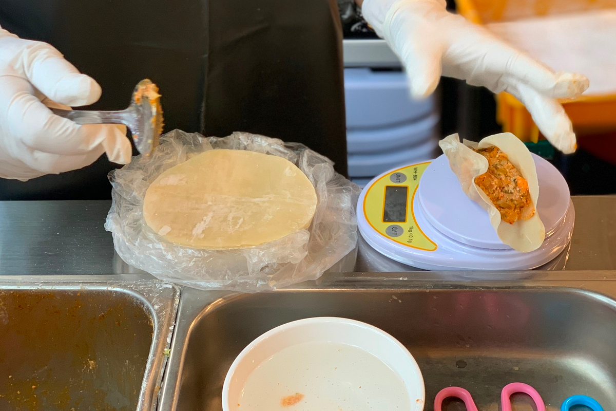 手工製作中的韓式餃子，工作人員正在仔細包裹餃子，展示了新鮮餃子的生產過程。