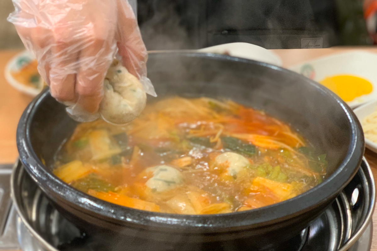 服務生在為顧客盛裝一盤熱氣騰騰的韓式牛肉湯和燒燙的火鍋食材互相搭配。