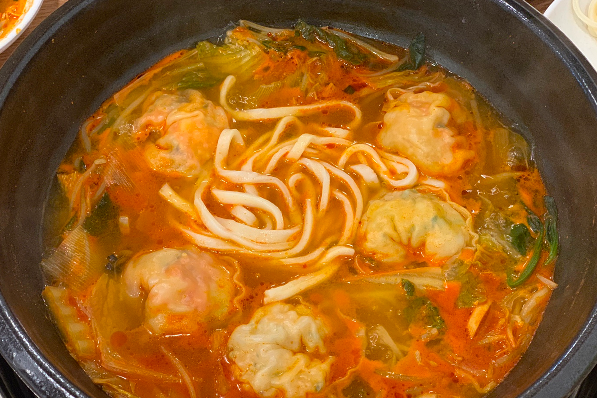 一個已經分開的韓式餃子，露出內餡的綠色蔬菜和香料，放於湯碗的頂端。