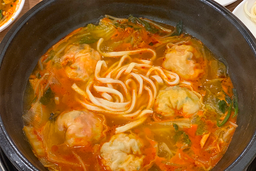 韓國首爾聖經餃子店的紅湯餃子鍋，餃子包裹著豐滿的泡菜和豬肉內餡，搭配刀削麵煮熟。