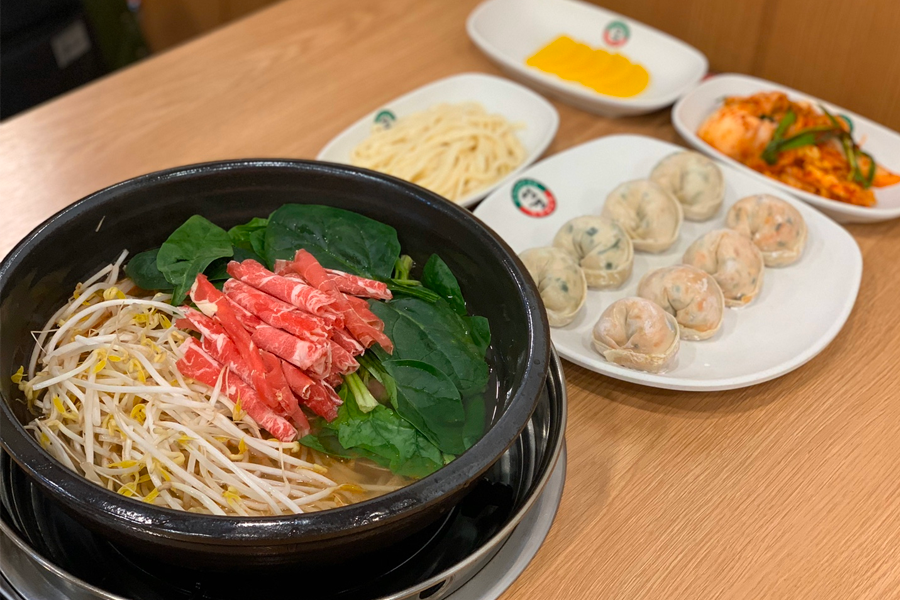 韓國首爾聖經餃子店的紅湯餃子鍋，搭配牛肉片與各種新鮮蔬菜。