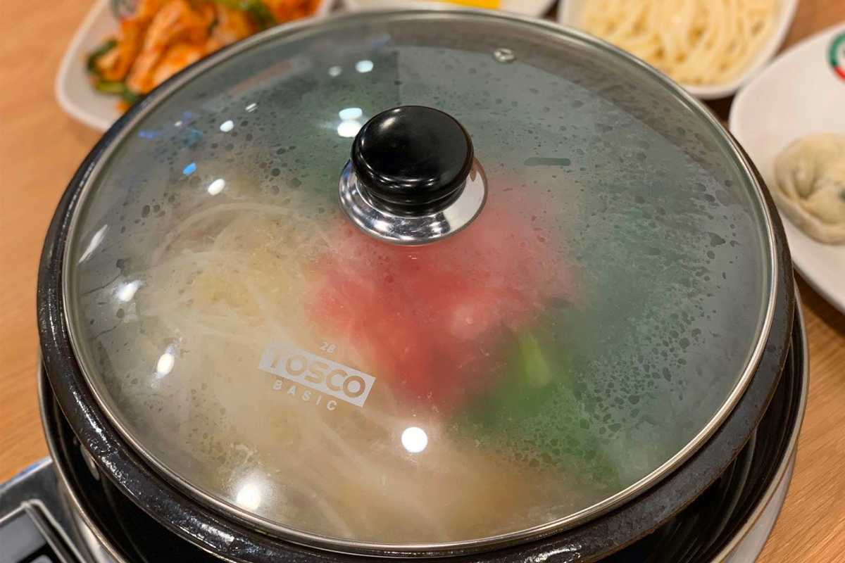 一份盛裝著生牛肉、餃子和菠菜的鮮美湯鍋，搭配著各式配菜，呈現出豐盛的韓國美食。