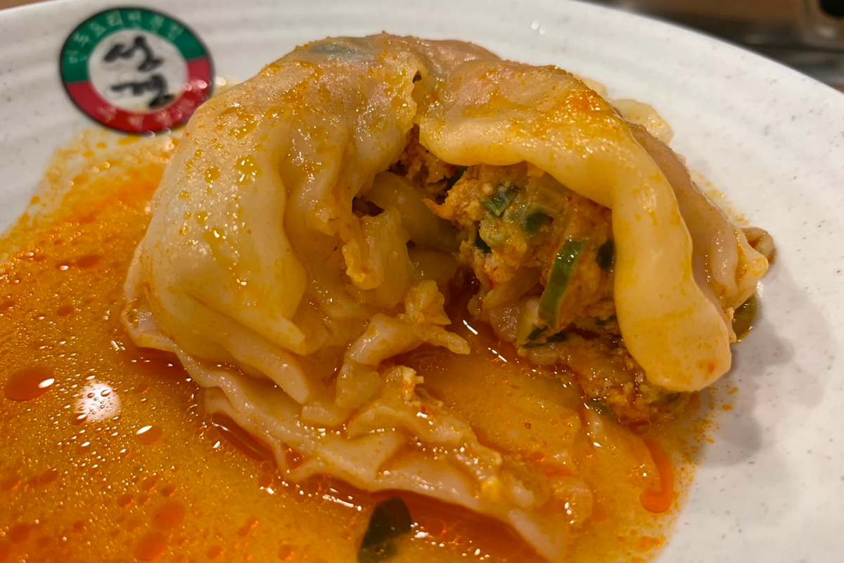 一份看起來美味可口的韓式飲食，滿滿的餃子和辛辣的湯底混合在一起，泡著各種食材。
