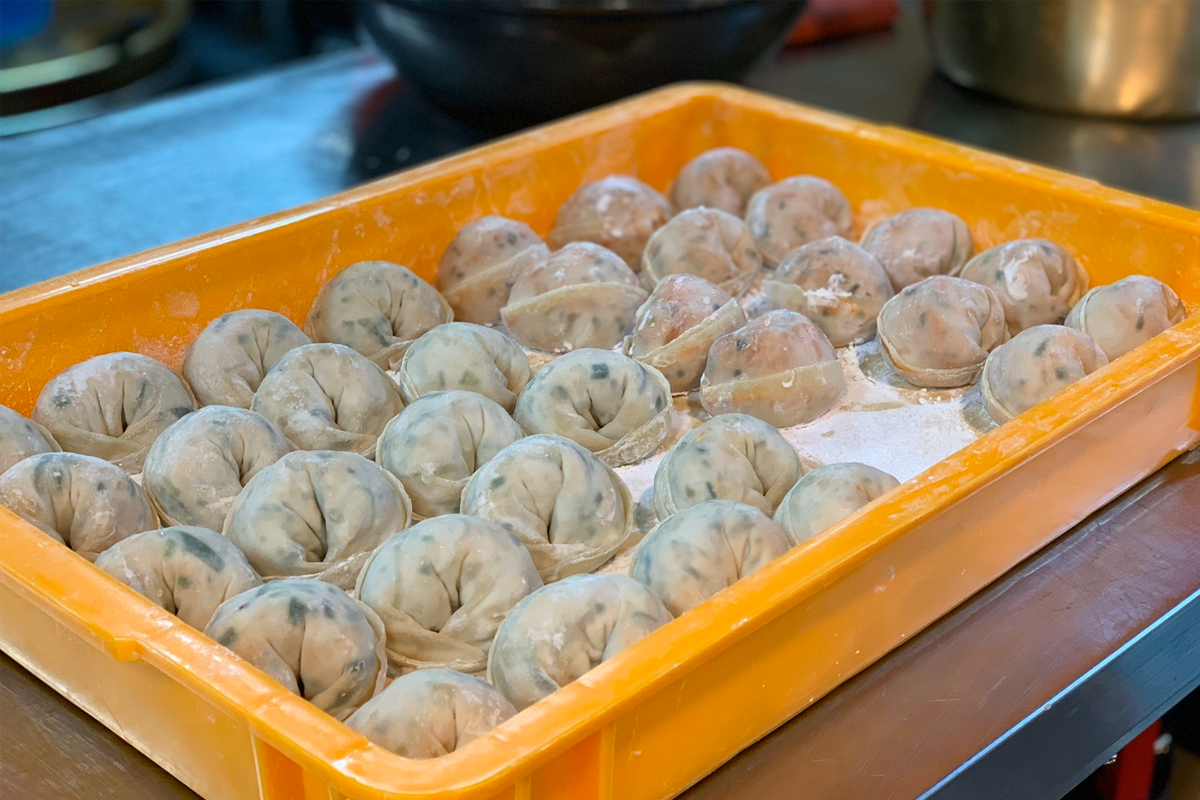 一個擺滿準備煮食的手工餃子的託盤，整齊排列並撒上一層薄面粉。