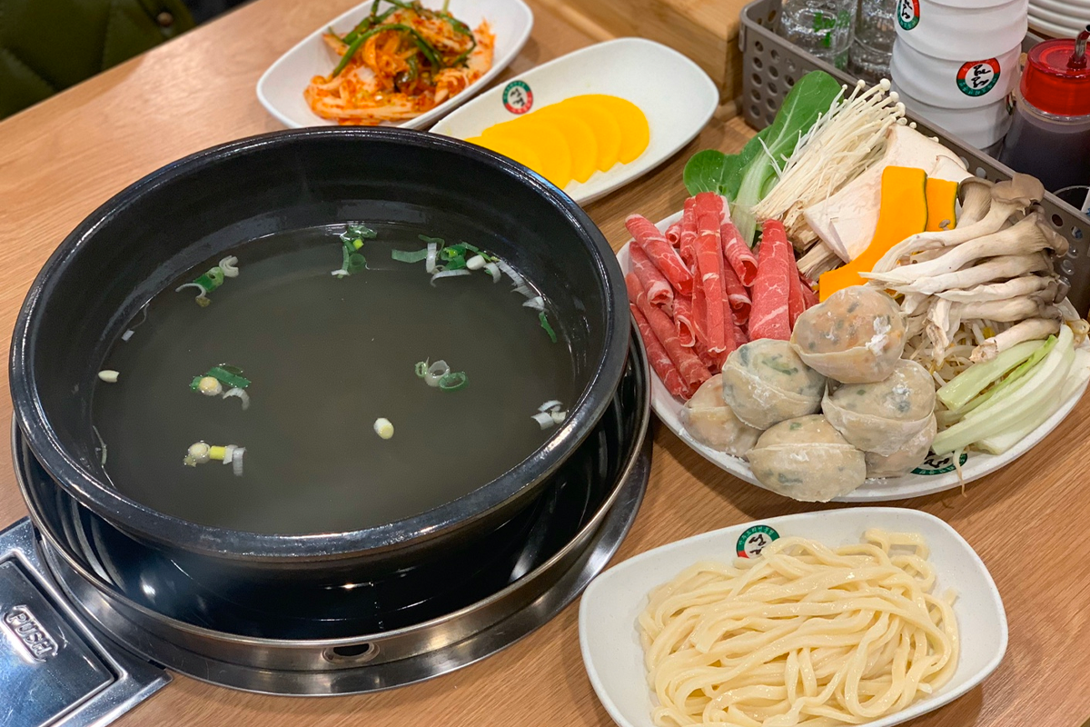 熱騰騰的湯鍋，內有煎餃和手工麵條，餃子翻滾在紅色的湯底中。