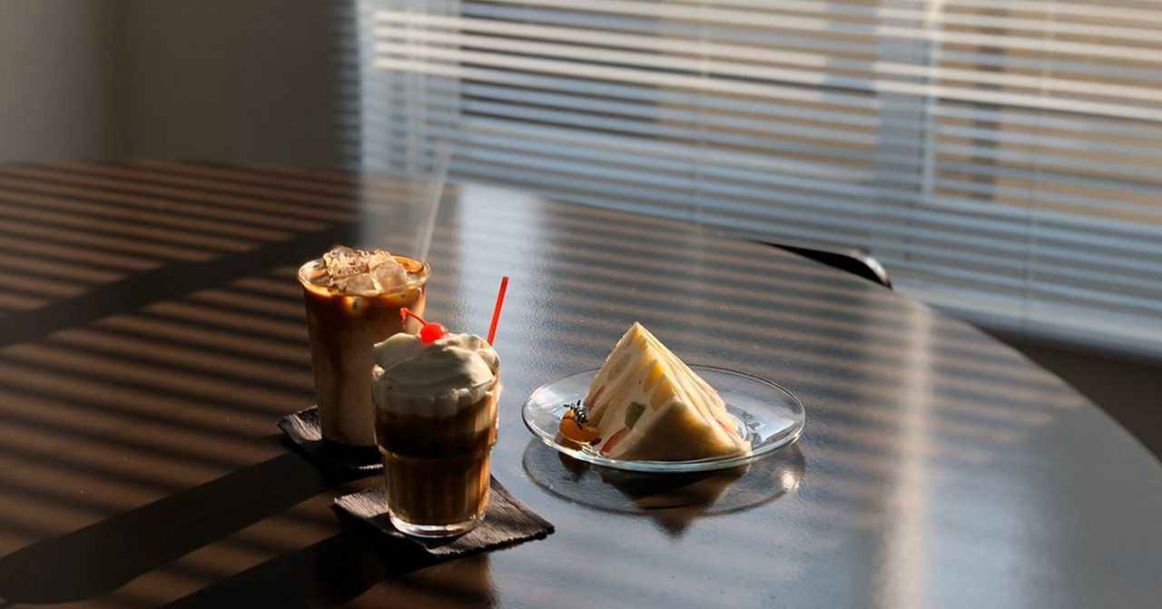 桌上的咖啡飲料與三明治，在陽光穿透百葉窗的溫馨氛圍中