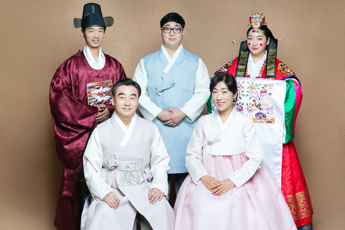 Lima orang mengenakan hanbok tradisional dalam sesi foto keluarga di studio dengan latar belakang polos.
