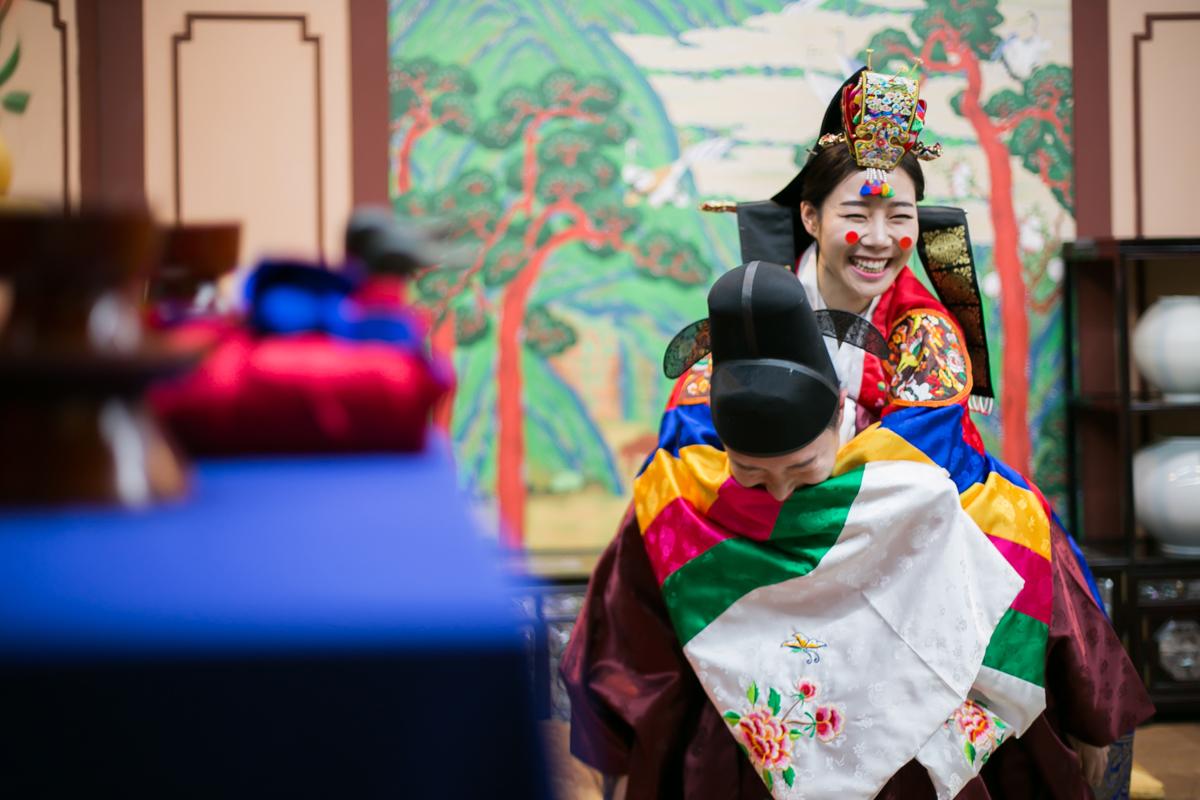 Pasangan dengan jubah tradisional Korea dalam upacara pernikahan dengan dekorasi tradisional di latar belakang.