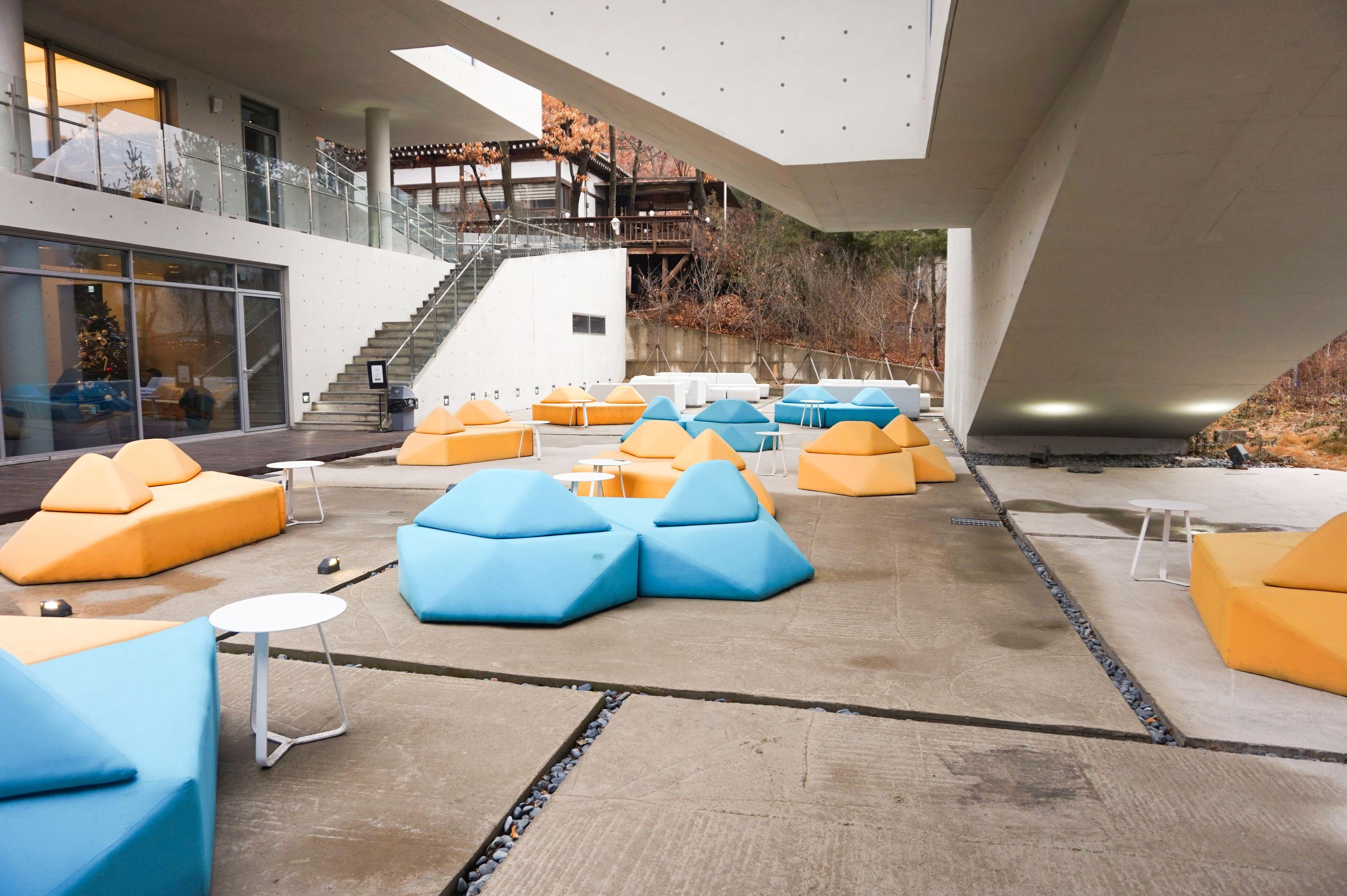 Außenbereich von GARDENUS in Paju mit bunten blauen und gelben Sofas vor minimalistischem Gebäudedesign.