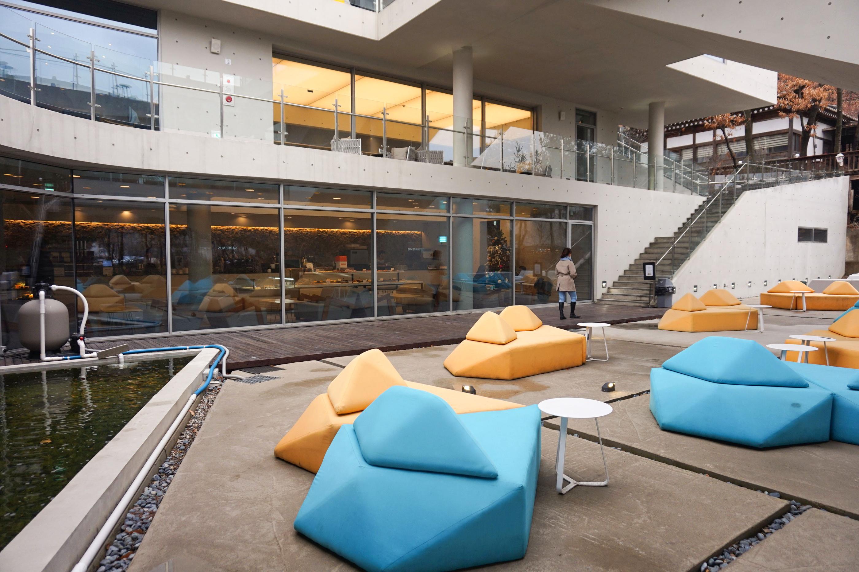 Unterer Hofbereich von GARDENUS in Paju mit stilvollen Sofas in Blau- und Gelbtönen.