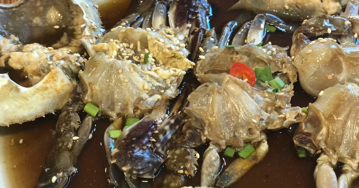 一盘鲜亮的韩式酱蟹（酱油蟹），上面撒有芝麻和青葱，装饰红辣椒片。