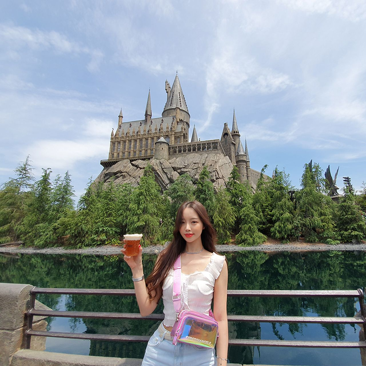 在哈利波特城堡的壯麗景緻前展示夏日搭配，肩袋顯現出鮮豔的粉色與童趣感。