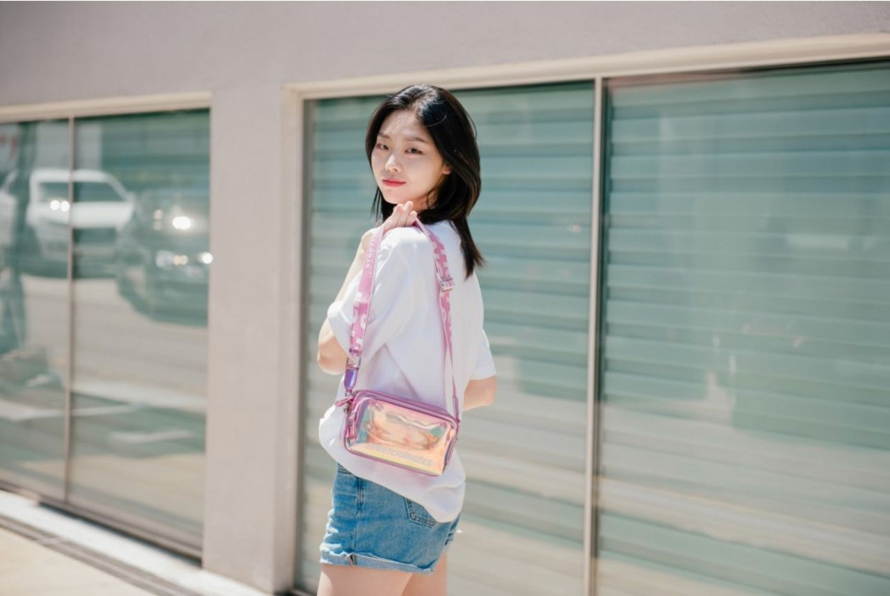 白色上衣與牛仔短褲搭配粉色透明手袋，漫步在時尚城市環境中。