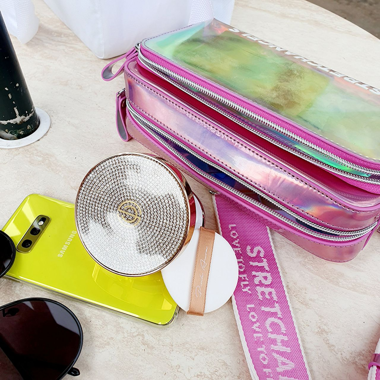 粉色拉鍊手袋擺放著手機與化妝鏡，高光鮮豔的色彩反射出流行時尚感。