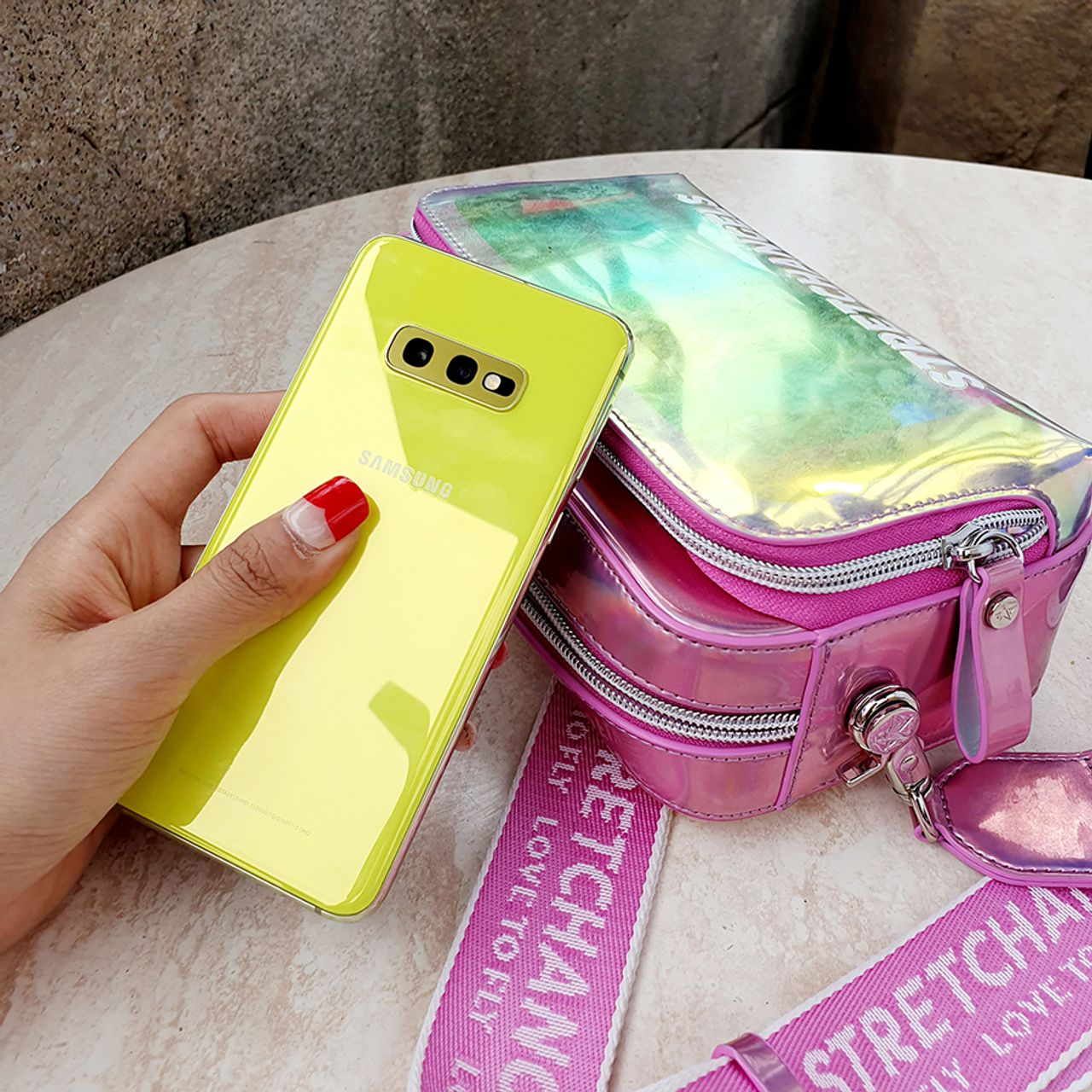 黃色手機靠近粉色透明包包，户外陽光勾勒出青春活力。