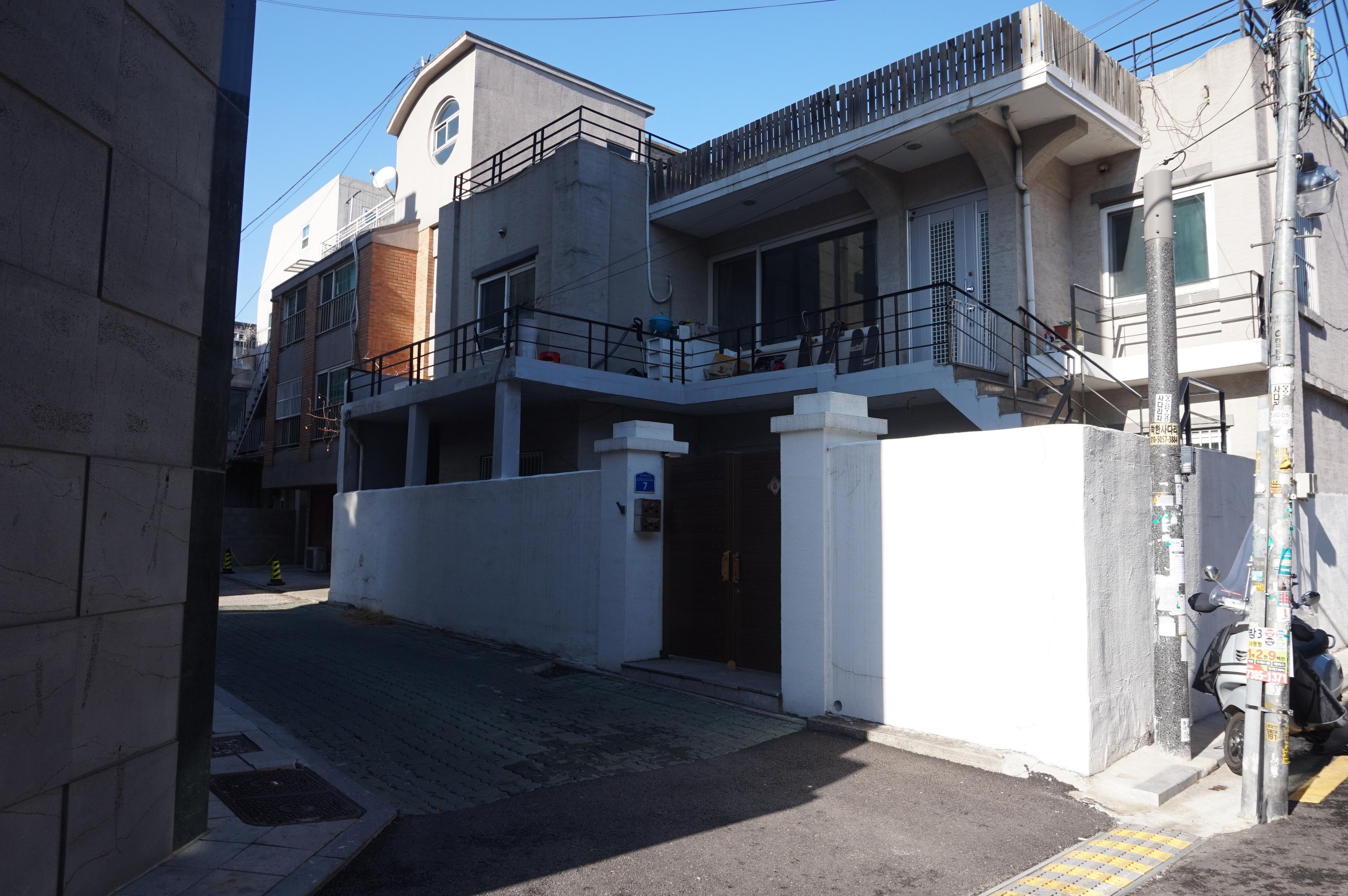 ソウルの道沿いにある白い壁の住宅建築物で、青空と調和している景観写真。