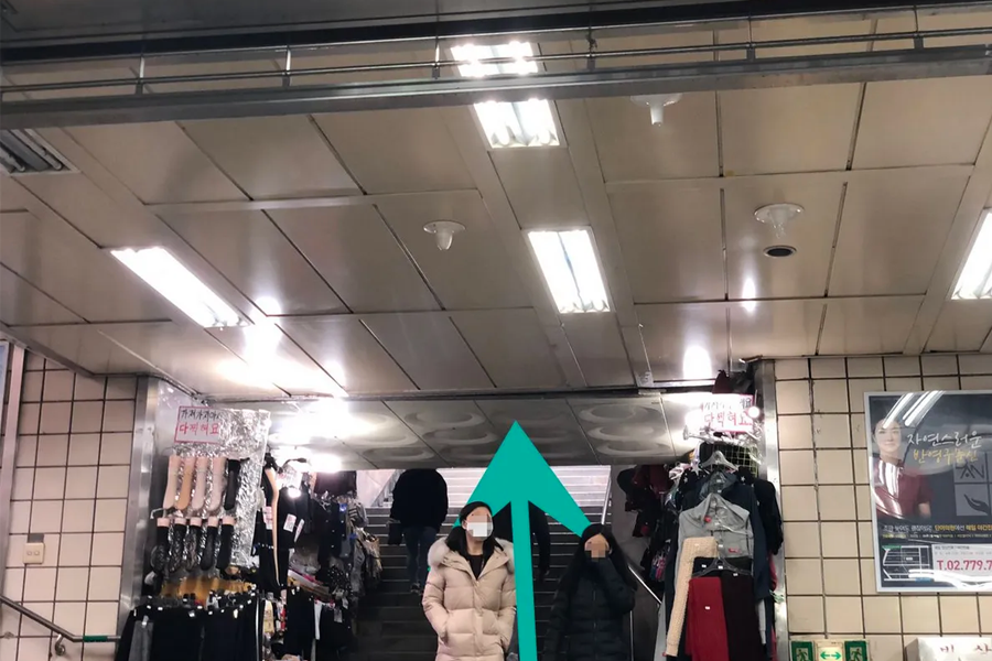 首爾繁忙街口，人行道上匆匆過客，周邊環繞著便利店和多樣商家。