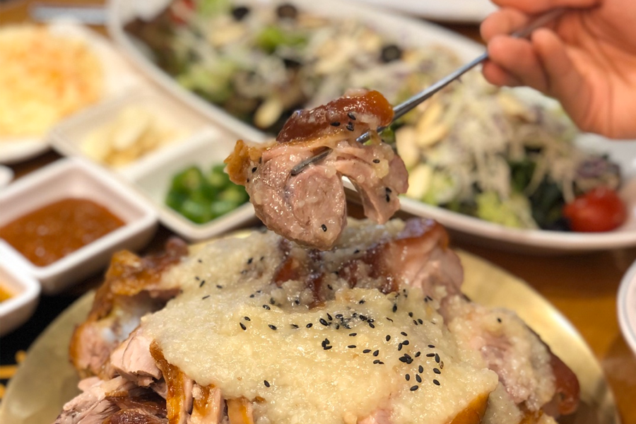 從碗中夾起的豬腳，覆蓋著蒜泥醬汁和黑芝麻，加強美味的視覺效果。