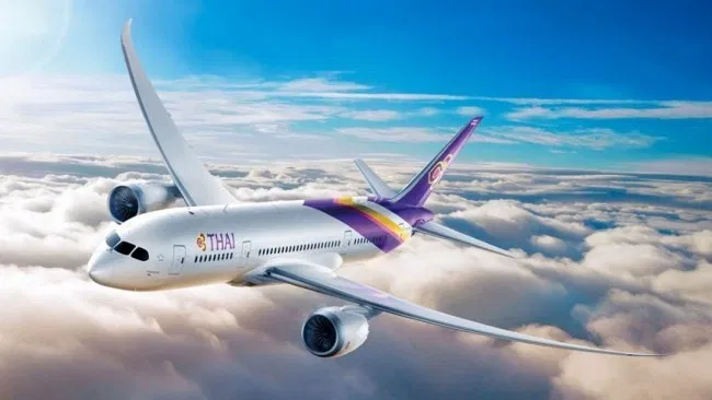 เครื่องบินของการบินไทยลอยอยู่ท่ามกลางเมฆบนท้องฟ้าสดใส พร้อมโลโก้สีม่วงบนหางเครื่อง 