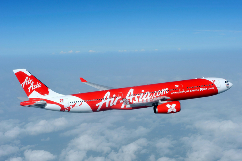 เครื่องบินของ Air Asia ที่มีโลโก้สีแดงสดใสบนหางเครื่องบิน กำลังแล่นผ่านท้องฟ้าสีฟ้า 