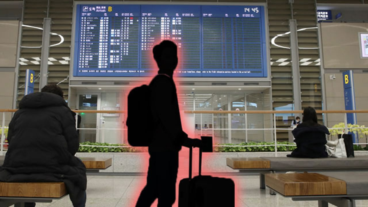 ภาพเงาของผู้โดยสารตรงหน้าจอเที่ยวบินที่สนามบิน ซึ่งกักไฟสีแดงที่ภาพเงา แสดงถึงการเดินทางที่ถูกจำกัด 