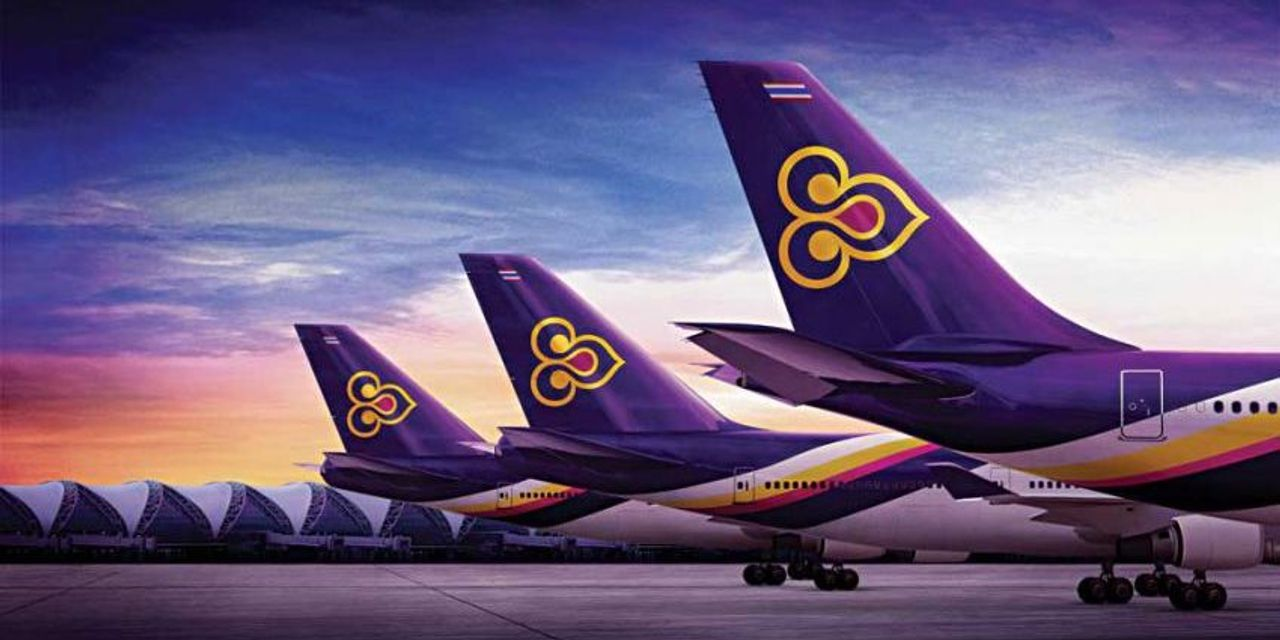 ภาพแถวของหางเครื่องบินการบินไทยที่ยืนเรียงราย โดยมีท้องฟ้าและสนามบินอยู่ด้านหลัง 