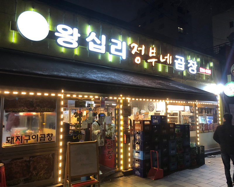 韓城市中心有名的烤腸店外景，店鋪門口燈火通明，招牌上顯眼的韓文字提醒路人美味在此。