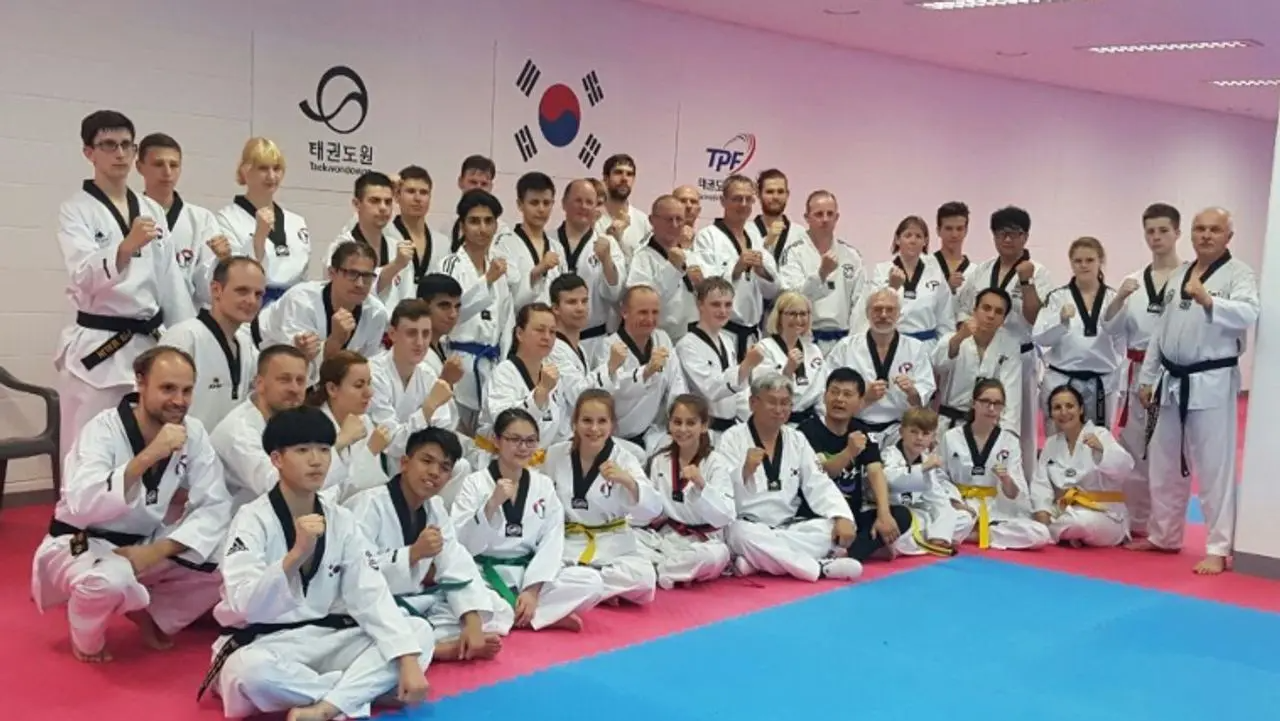 一群學員在跆拳道道場內合照，大家穿著跆拳道服裝，背景有韓國國旗和牆上的標誌