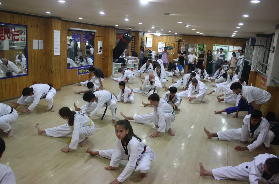 穿著軍裝的學員們在室內體育館接受跆拳道教練的訓練，牆上有韓國和美國國旗