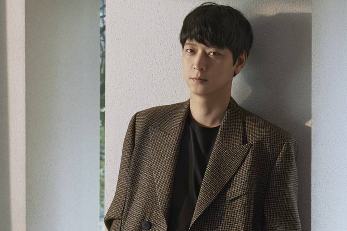 姜棟元穿著格子西裝，在建築物中的側身照片。