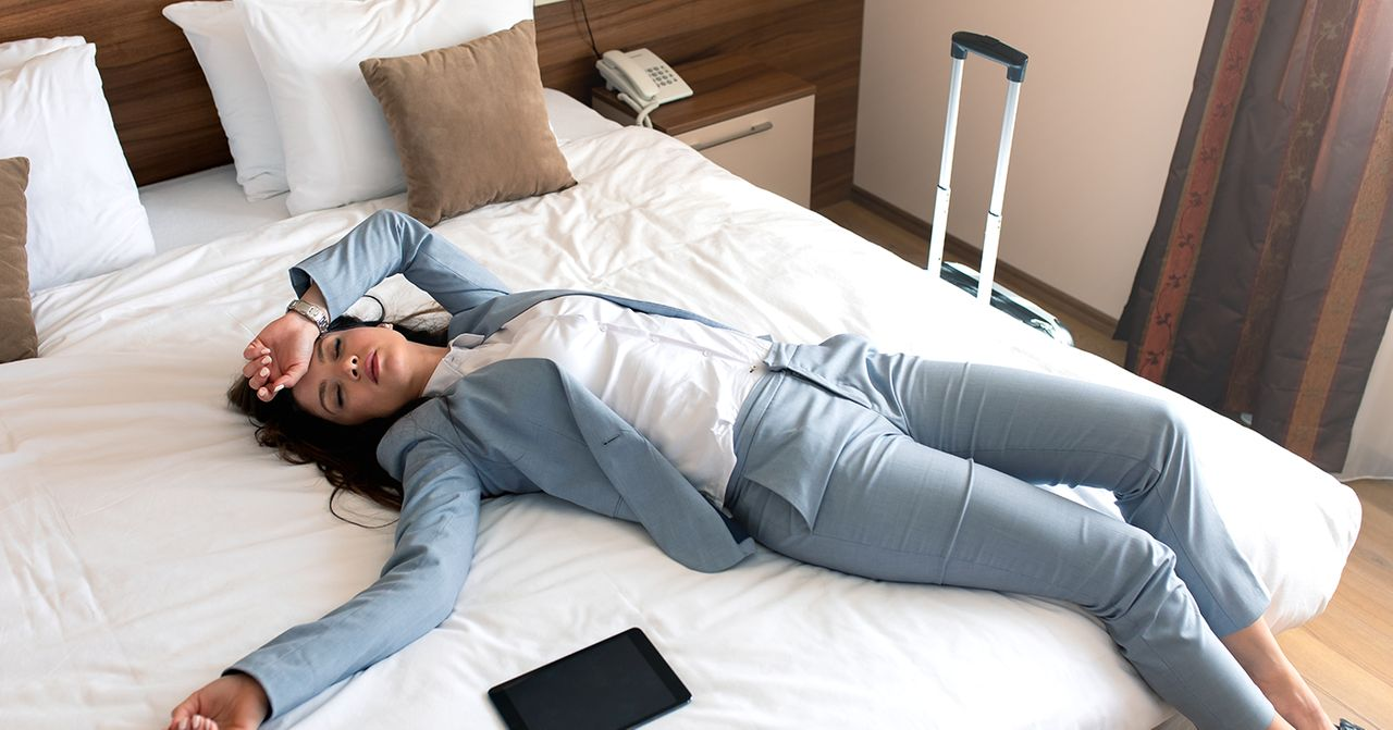 一名身穿藍色西裝的女士躺卧在酒店牀上，顯出疲憊的樣子。