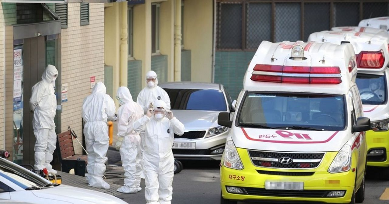 醫護人員全身穿著防護服準備進入建築內檢測病人，顯示韓國對疫情的緊急應對措施。