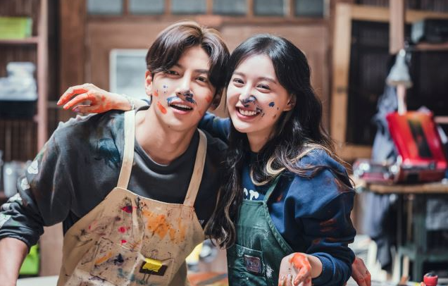 韓国ドラマ『都市の男女の愛し方』の一場面。アートをテーマにしたカフェで二人のキャラクターが楽しげに色を混ぜ合わせている。軽やかで自由な雰囲気が漂っている。