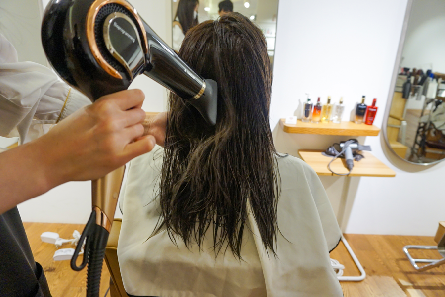 髮型師在吹乾顧客的濕髮，使用吹風機技巧讓髮型更自然柔順。