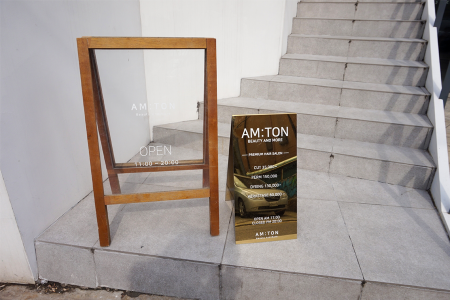 AM:TON 髮廊的營業時間招牌和價格表，顯示其營業時間和服務價格。拍攝於髮廊外的樓梯旁。