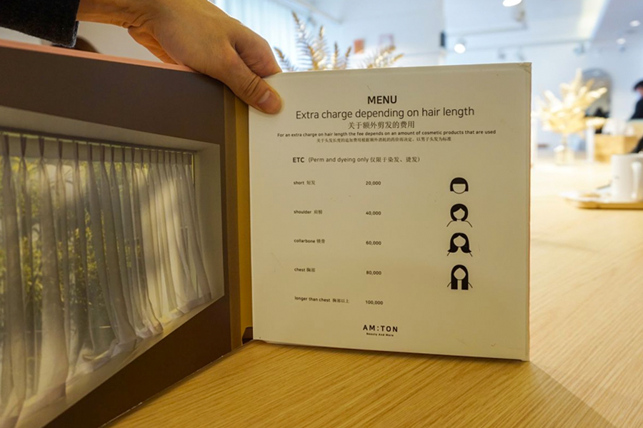 顧客查看 AM:TON 髮廊的髮型服務價目單，手持價目表，方便顧客瞭解服務費用。