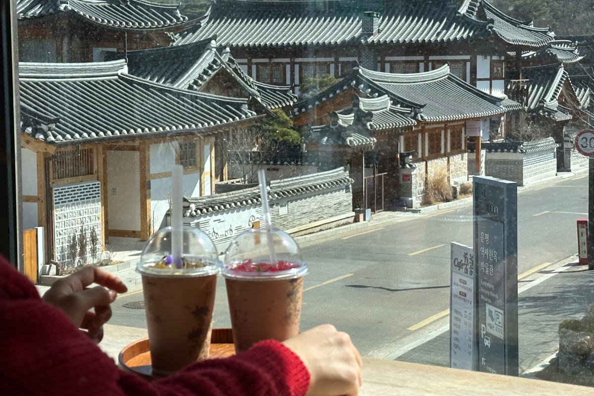 Two blended drinks placed on a table by the window in 1 In 1 Jan cafe, overlooking the traditional architecture of Eunpyeong Hanok Village.