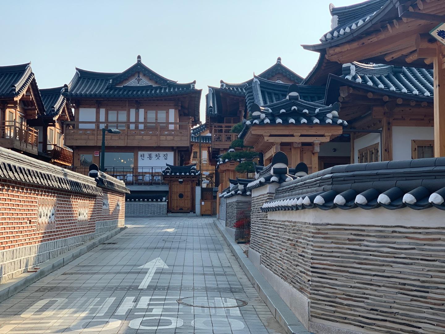 Pathway leading through Eunpyeong Hanok Village surrounded by traditional hanok structures with intricate details and a clear blue sky overhead.