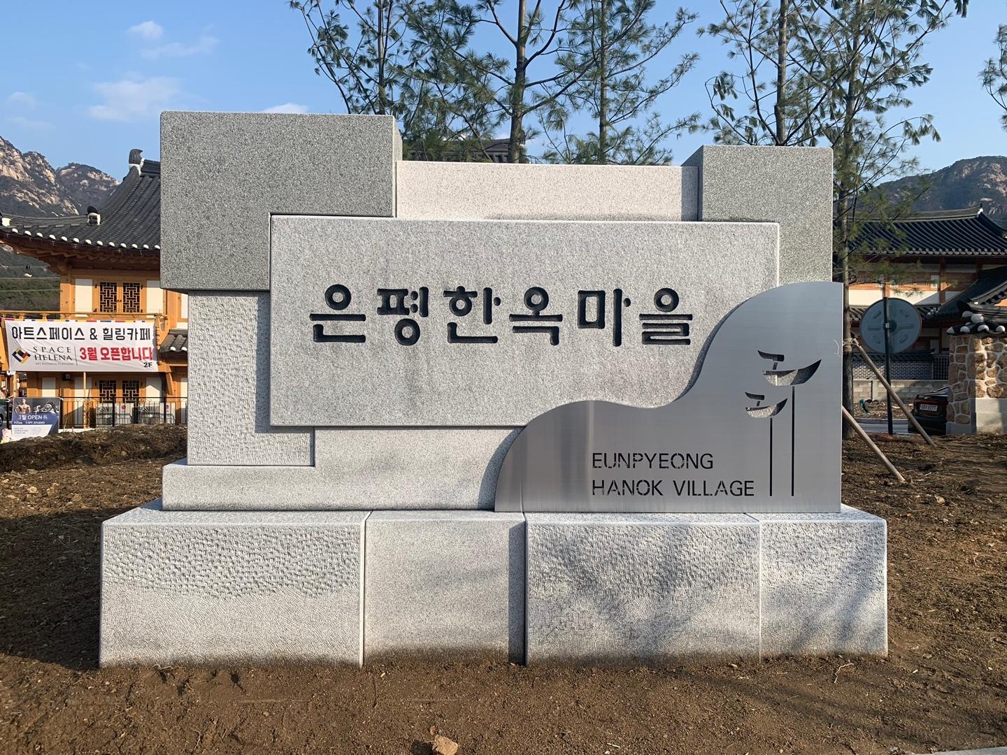 Entrance sign of Eunpyeong Hanok Village with traditional Korean architecture in Seoul, South Korea. Mountains are visible in the background under a clear sky.