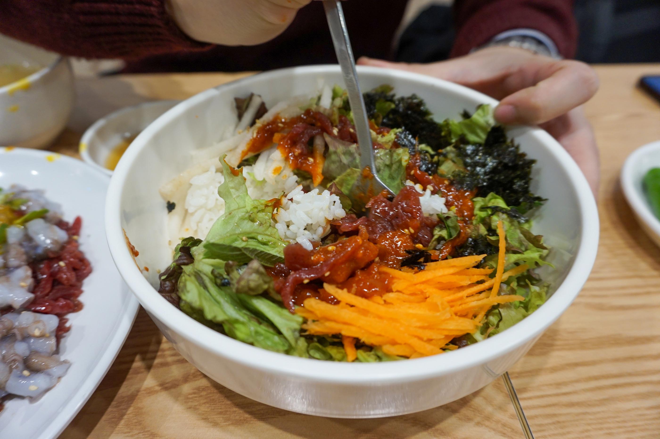 ユッケビビンパの食材の一部をスプーンで取る様子。色鮮やかな具材が混ざっている。