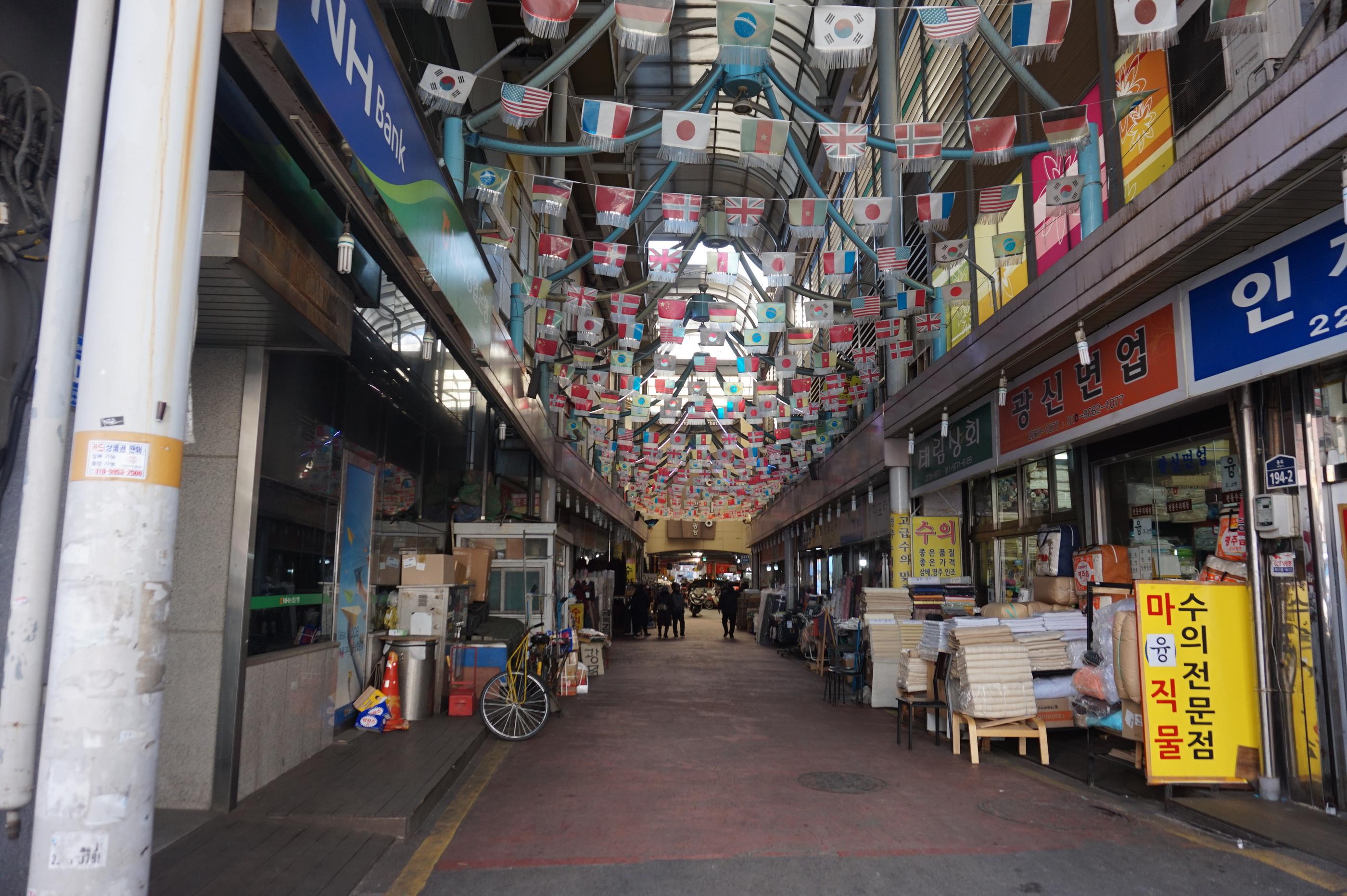 各国の国旗が天井に飾られた広蔵市場の入口。左右に並ぶ店舗が見える。