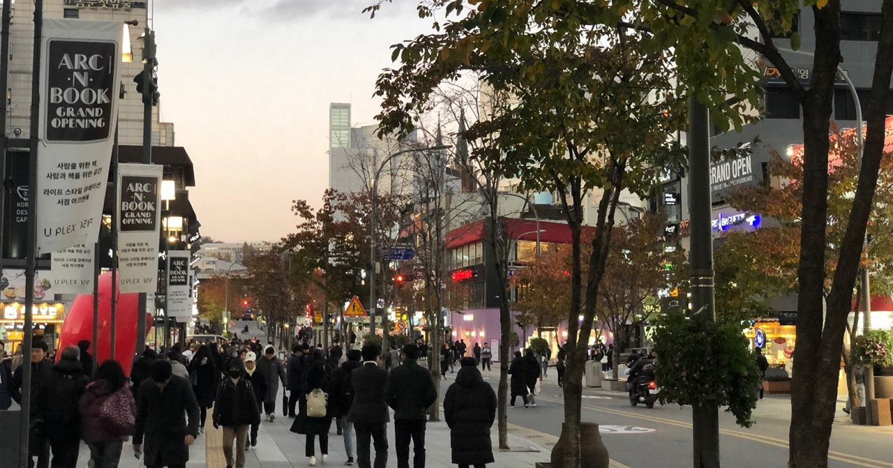 新村商圈晚間街景，行人來來往往，街道兩旁的店舖和樹木彰顯出活力的氛圍