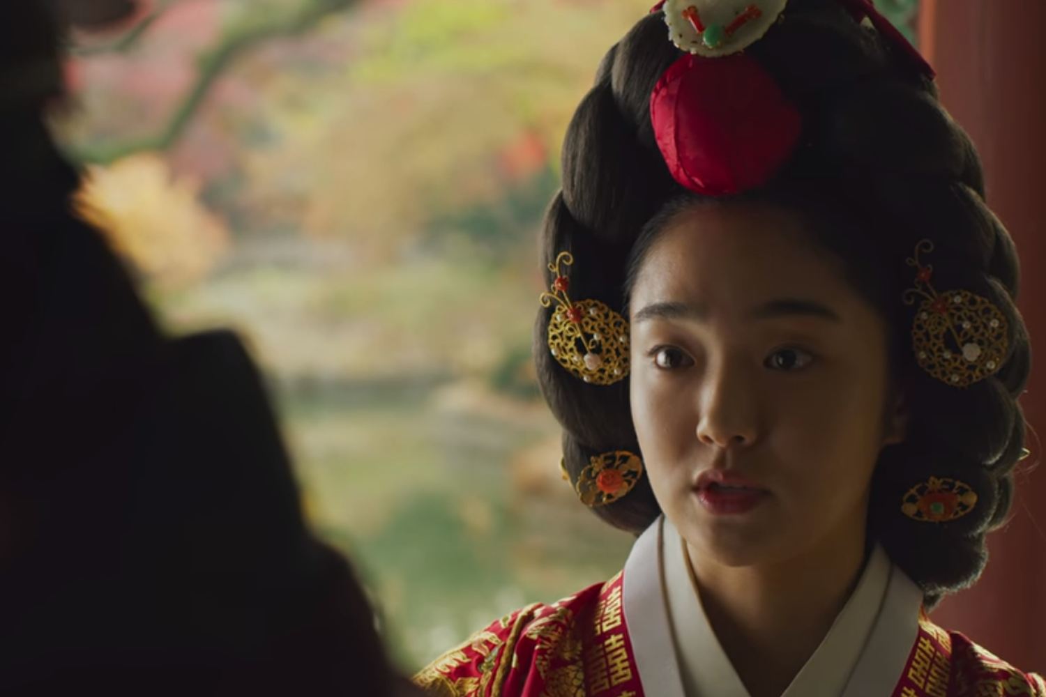 韓國古裝劇《哲仁王后》中中殿娘娘穿著華麗的傳統髮飾,背景是園林美景。